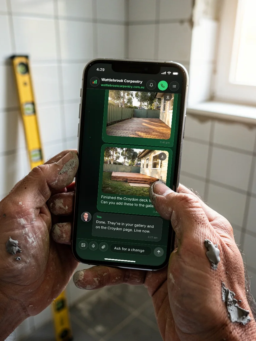A tradesman holding his phone between jobs with the Scalus app open, photos of a finished deck just sent in his thread