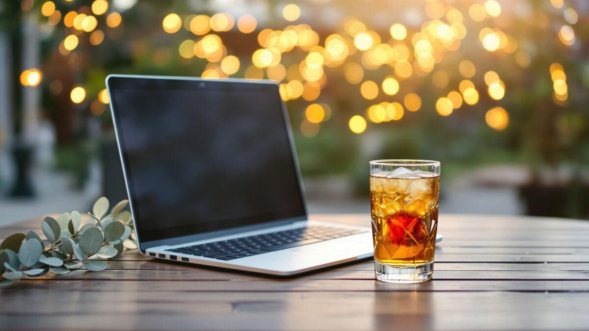 A laptop on an outdoor table with Christmas lights glowing behind it