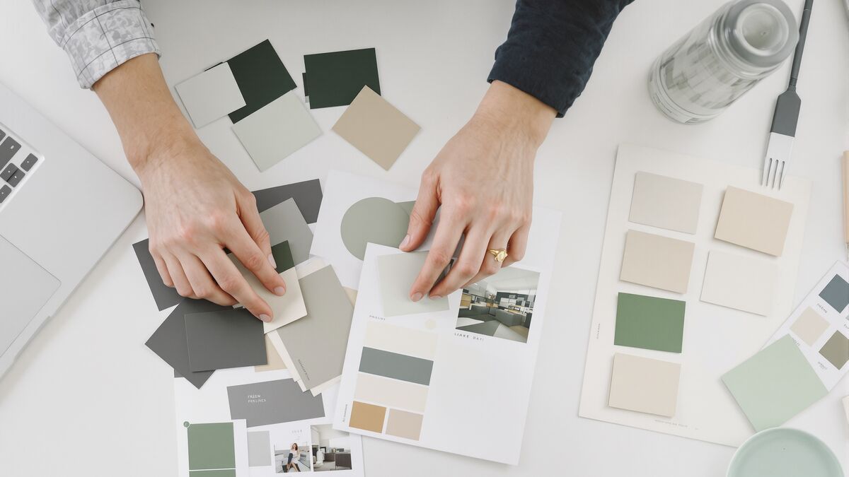 Hands laying out colour swatches and page layouts beside a laptop