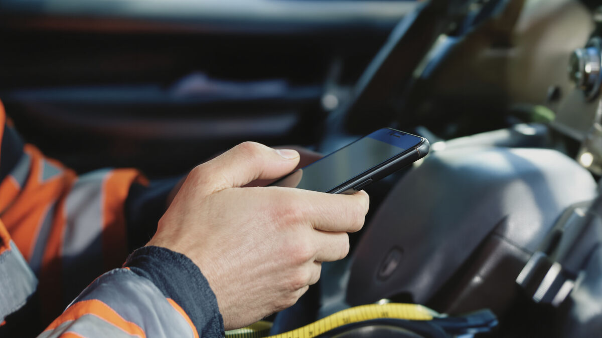 A tradesman in a work ute typing a message on his phone