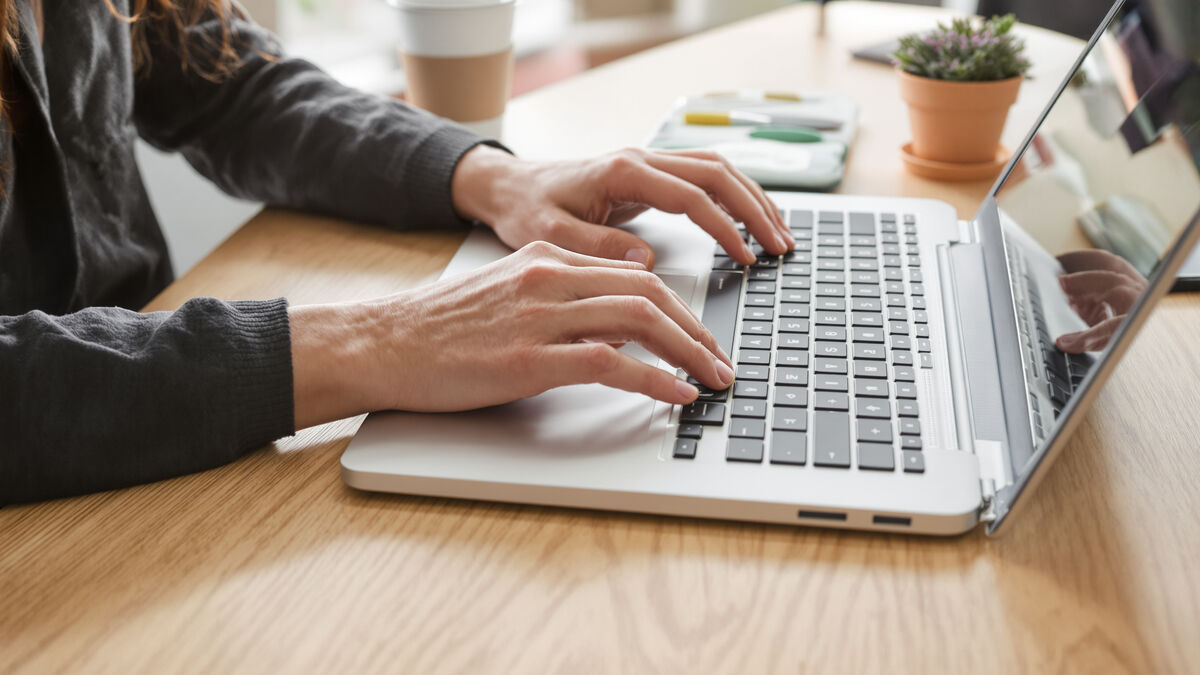 Hands typing on a laptop at a timber desk