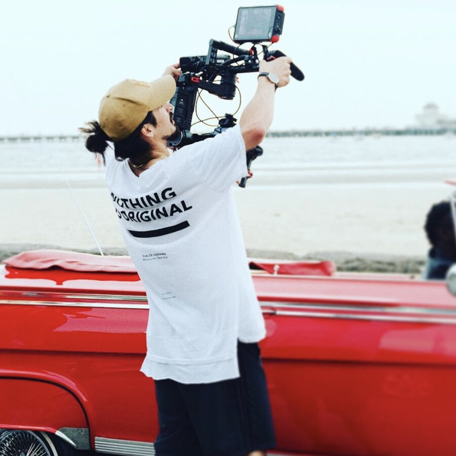 Tim McCartney filming beside a red classic car at the beach