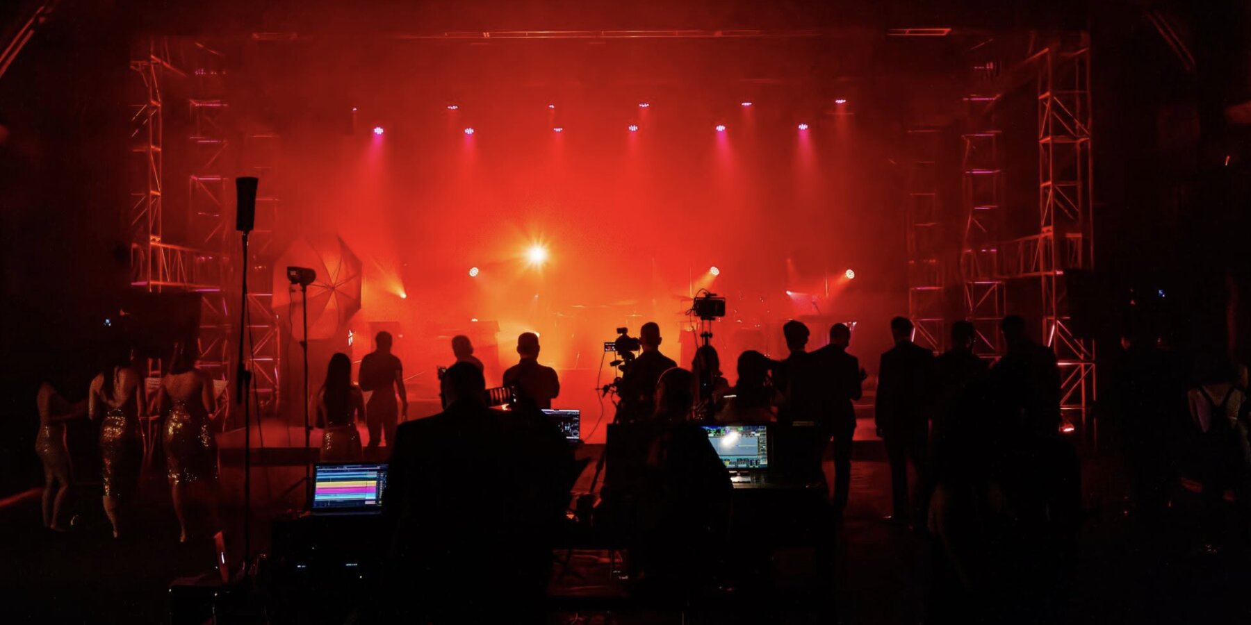 A live production in progress, crew and monitors in front of a lit stage